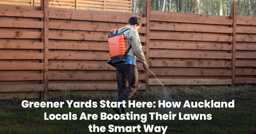 Auckland professional applying lawn fertilizer using a backpack sprayer near a wooden fence.